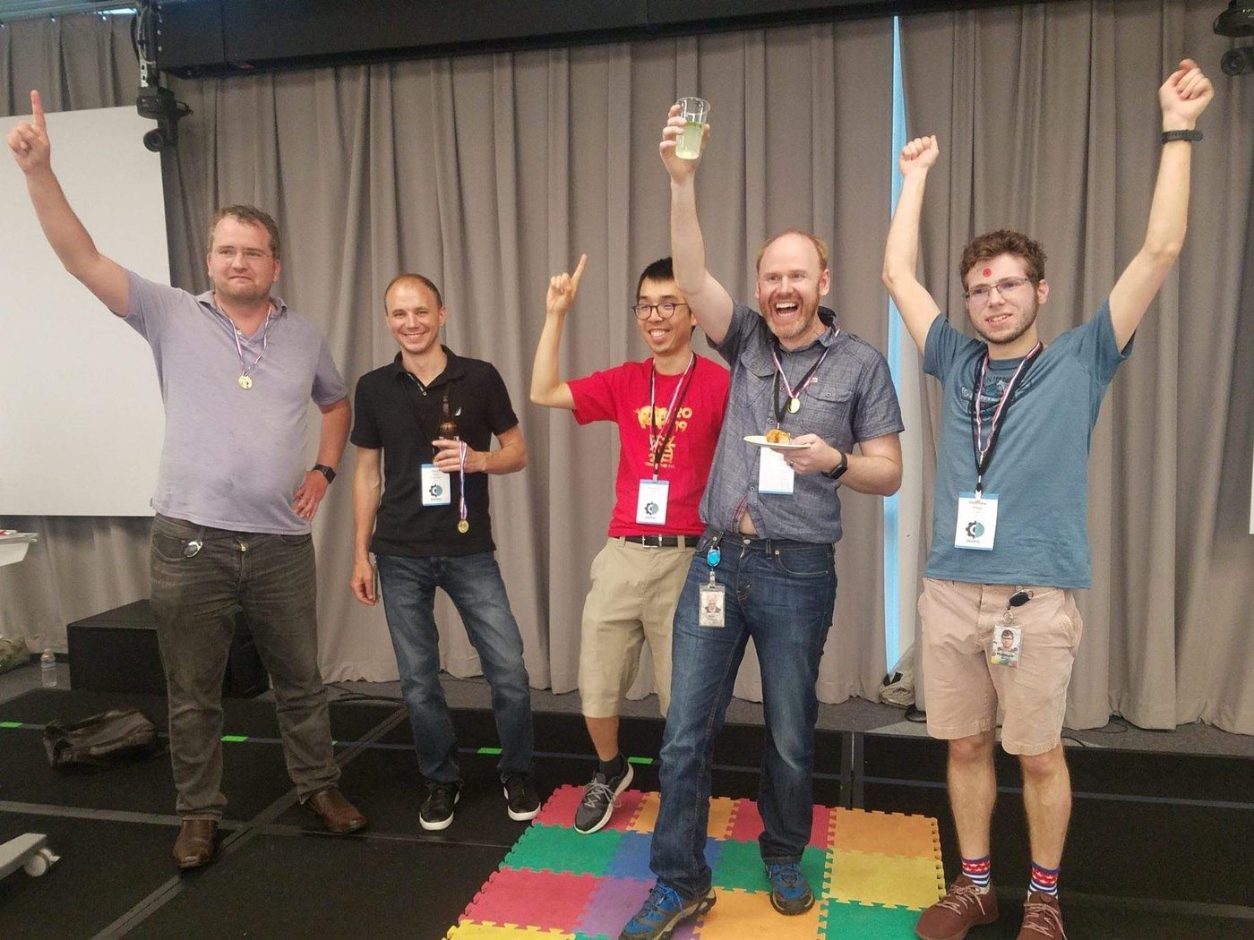 Five teammates celebrate with medals and raised arms after their game show